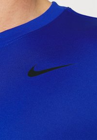 Närmre bild av en person som bär en blå sporttröja med en svart Nike-swoosh-logotyp nära halslinningen.