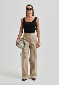 Top aderente nero, pantaloni beige a vita alta, calzature nere con texture e una borsa a tracolla grigia con stampa a serpente.