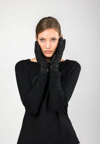 Guanti neri con superficie texture e dettagli in bianco, indossati da un modello. Il modello indossa una maglietta nera a maniche lunghe.
