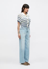 Cárdigan de punto con rayas azules y crema, mangas cortas, cierre de botones. Vaqueros de corte holgado en azul claro, combinados con zapatos de estampado de leopardo.