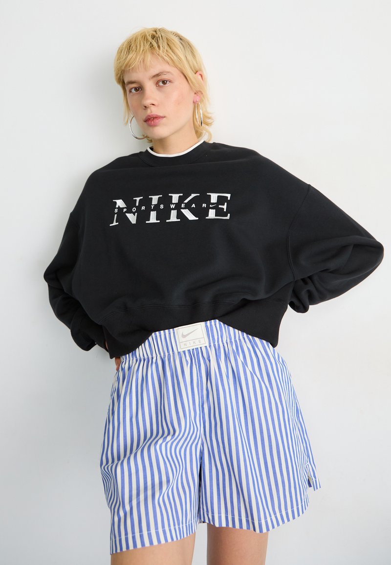 Czarna bluza z kapturem z białym napisem "NIKE", w połączeniu z niebieskimi i białymi spodenki w paski z elastycznym pasem i metką z logo.