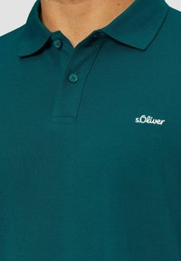 T-Shirt in Türkis aus strukturiertem Stoff mit Kragen, ausgestattet mit einer Knopfleiste mit zwei Knöpfen und kleinem gesticktem Logo auf der Brust.
