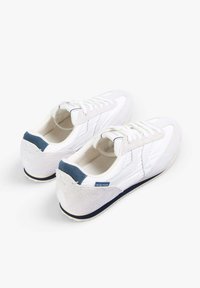 Zapatillas blancas con una mezcla de cuero liso y ante, que presentan un acento en el talón azul, punta redonda y cierre con cordones. Detalle sutil del logo.
