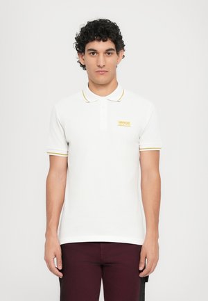 Hvit polo-skjorte med korte ermer som har gul kant, en klassisk krage, og en liten brodert logo på venstre bryst.