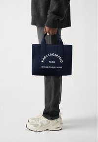 Navy blue tote bag made of fabric, featuring white text: "KARL LAGERFELD PARIS 21 RUE ST-GUILLAUME," with two sturdy handles.