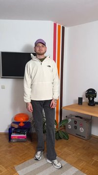 Sweatshirt branca em tecido polar com meio fecho e logótipo, combinada com jeans escuros e ténis cinzentos. Os acessórios incluem um boné roxo.