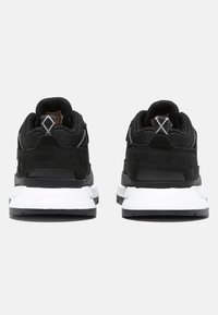 Zapatillas deportivas negras con una parte superior de malla texturizada y acentos de ante. Presentan una media suela blanca y una lengüeta de tirón en el talón con un patrón.