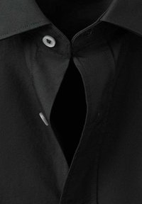 Camisa negra con cuello clásico, cierre con botón blanco y textura de tela suave. Detalle notable de recorte en el cuello.