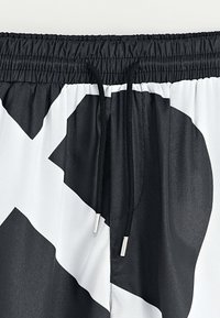 Shorts de bain noirs et blancs avec un motif géométrique, dotés d'une taille élastique et d'un cordon de serrage avec embouts en acier pour un ajustement réglable.