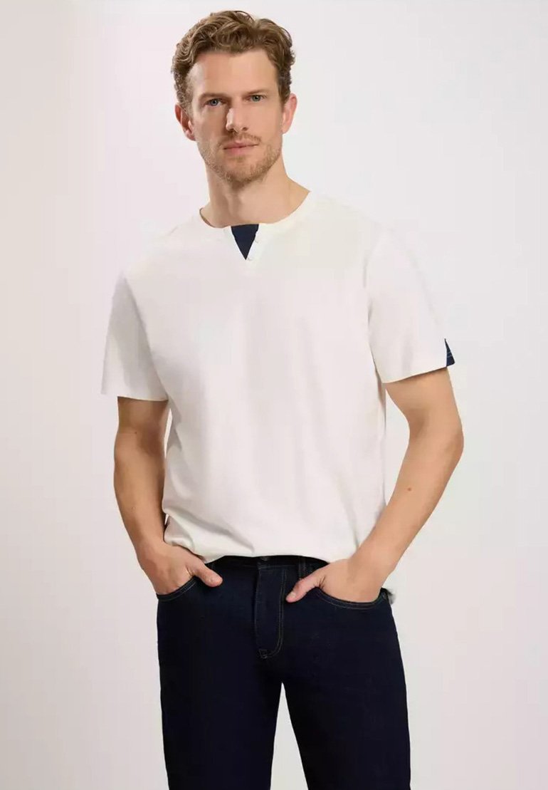 Biała koszulka z krótkim rękawem z granatowym akcentem przy dekolcie, w połączeniu z ciemnoniebieskimi dżinsami. Tkanina wydaje się gładka i lekko teksturowana.