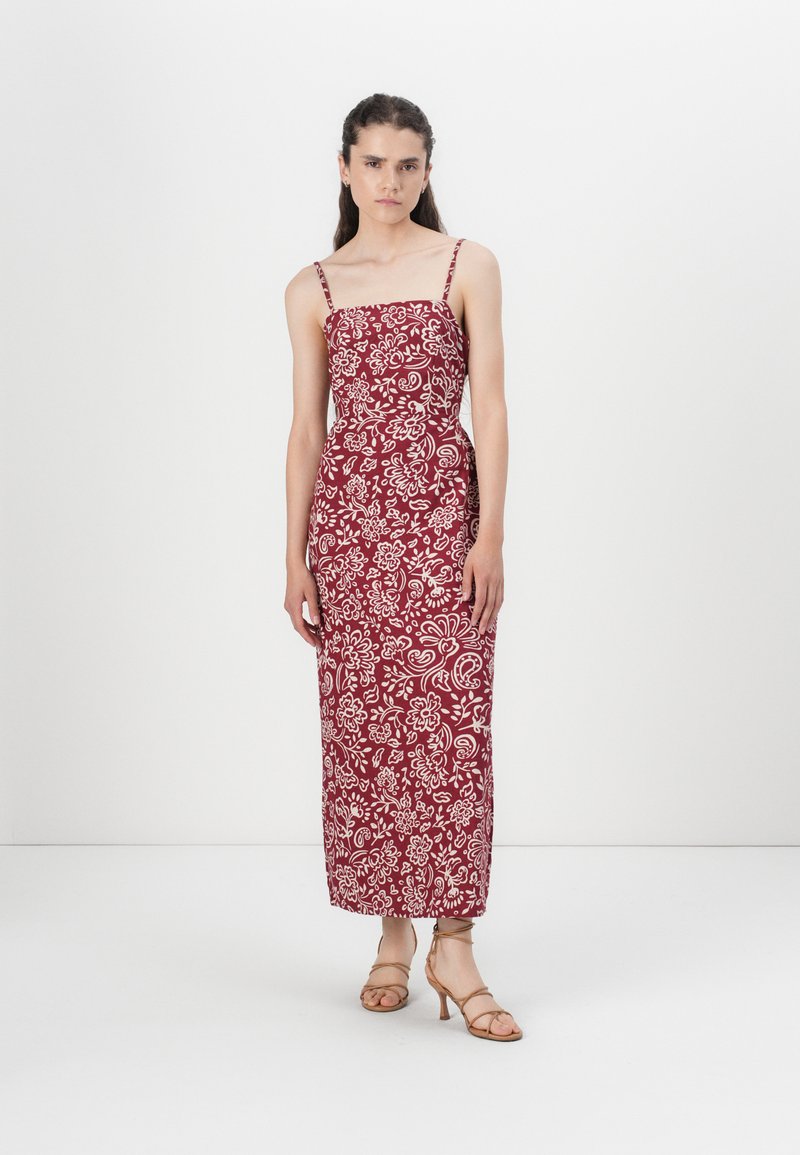 Röd mönstrad maxi-klänning med tunna axelremmar, prydd med vita blommönster. Tyget ser lätt ut och kompletteras med sandaler med remmar.