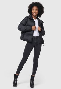 Schwarze Pufferjacke mit Reißverschluss vorne, hohem Kragen und gerippten Bündchen, kombiniert mit enganliegenden schwarzen Jeans und Stiefeletten.