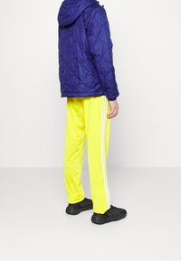 Marinblå puffjacka med huva, kombinerad med ljusgula träningsbyxor med vita sidor, och svarta sportskor.