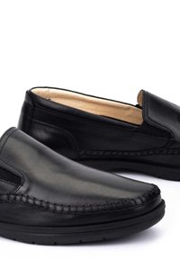 Zapatos de cuero negro tipo mocasín con textura suave, detalle de costura contrastante, punta redondeada y forro interior suave. Presentan un diseño minimalista.