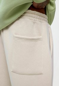 Beige trainingsbroek met een zachte textuur, voorzien van een elastische tailleband en een enkele achterzak met gestikte details.