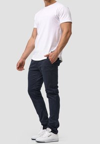 Vit bomulls t-shirt, marinblå slim-fit byxor och vita sneakers. T-shirten har en rund halsringning; byxorna har fickor och en slät yta.