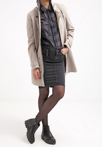 Grå ullblandad kappa över en svart denimkjol och mönstrad skjorta, ihop med svarta ankelstövlar. Släta texturer, skräddarsydd passform.