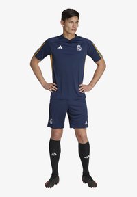 Uniforme de fútbol azul marino, camiseta de manga corta con detalles en amarillo, pantalones cortos a juego, calcetas negras y botines negros. Cuenta con el logotipo del club y rayas.