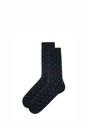 Calcetines negros hasta la mitad de la pantorrilla con pequeños lunares azules uniformemente distribuidos, colocados planos uno al lado del otro sobre un fondo blanco.