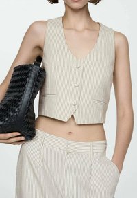 Beige striped cropped vest with a V-neck and three buttons, paired with matching high-waisted striped trousers and a textured black bag.