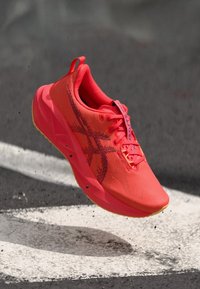 Helles oranges Sportschuh mit einem strukturierten Obermaterial, fettem schwarzen Logo und gelber Sohle. Verfügt über ein Schnürsystem und eine Schlaufe für einfaches Anziehen.