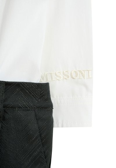 Biała koszula z haftem "MISSONI" w kolorze kremowym, zestawiona z czarnymi spodniami teksturowanymi w wzór jodełki.