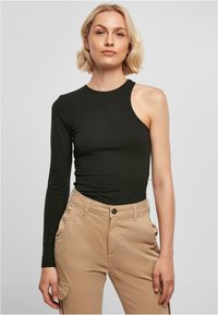 Svarte langermede topp med en skulderutskjæring, laget av elastisk materiale. Fitted design med rund halslinning. Kombinert med beige bukser.