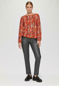 Rood en zwart slangenprint langlijf top, gecombineerd met glanzende zwarte slim-fit broek en dikke zwarte schoenen. Eenvoudig, modern ontwerp, zonder zichtbare patronen.