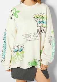 Sudadera extragrande color crema con texto y gráficos de estilo graffiti en verde y azul, con cuello y puños acanalados.
