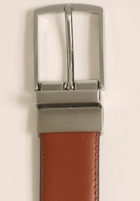 Rjav usnjen pas z pravokotno srebrno kovinsko sponko. Sponka ima eleganten dizajn in preprost zatič.