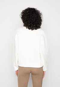 Vit sweatshirt med avslappnad passform, sänkta axlar och ribbade ärmslut, ihopparad med bruna tajta leggings. Slät textur och minimal design.