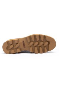 Suela de zapato de goma con una superficie texturizada; presenta grandes botones redondeados para tracción; color marrón claro; bordes suaves y una construcción sólida.