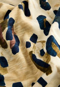 Látka s leopardím potiskem obsahující velké modré, hnědé a béžové tvary na jemném smetanovém pozadí s jemně texturovaným povrchem.
