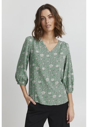 Blusa verde con motivo floreale, scollatura a V e maniche a tre quarti. Caratterizzata da una vestibilità ampia e da un materiale morbido e leggero.