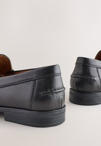 Mocassins en cuir noir à finition texturée, bouts arrondis et semelles en caoutchouc. Présentent des coutures décoratives et des accents en relief sur le talon.