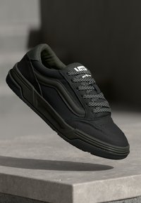 Zwarte sneaker met groene accenten, bovenwerk van textuurstof, gewatteerde kraag en gestippelde veters; gevormde zool met opvallende zijdetails.