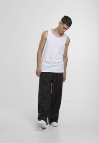 Valge puuvillane tank top, mida on paaritatud vaba lõikega tumehallide pükstega, millel on lihtne disain ja minimalism.