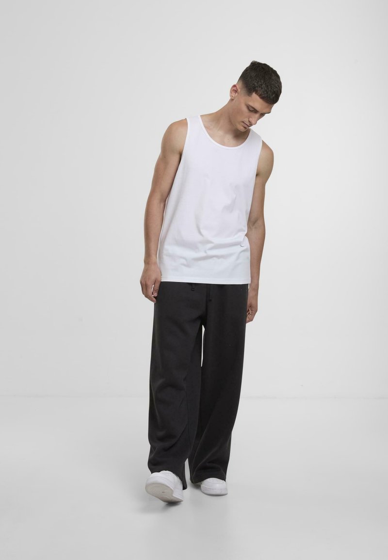Valge puuvillane tank top, mida on paaritatud vaba lõikega tumehallide pükstega, millel on lihtne disain ja minimalism.