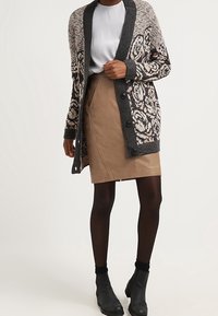 Sweter kardigan z dzianiny z kwiatowym wzorem w kolorach czarnym i kremowym, zestawiony z brązową skórzaną spódnicą. Czarne botki za kostkę dopełniają stylizację.