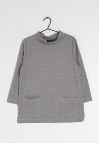 Šedý dlouhý rukáv s vyvýšeným límcem, který má texturovaný rybí kost a dvě přední kapsy. Vyrobeno z měkké tkaniny.