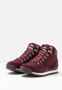 Dieprode wandelschoenen met een bovenwerk van suède en stof, metalen veterogen en contrasterende veters. De rubberen buitenzool heeft een gestructureerd profiel voor grip.