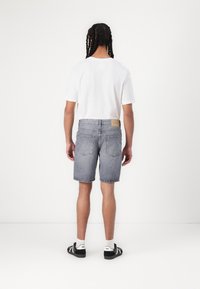 Shorts en denim gris avec une coupe droite et un ourlet effiloché, associés à un t-shirt blanc à col rond et des baskets noires avec des accents blancs.