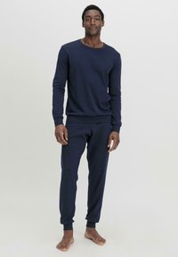 Marineblaue Baumwoll-Loungewear-Garnitur mit einem Langarm-Oberteil im Crew Neck und schmal zulaufenden Hosen, beide mit gerippten Bündchen und einer glatten Textur.