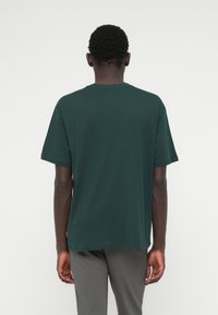 Tume roheline lühikeste varrukatega T-särk, mis on valmistatud puuvillast, sellel on ümar kaelus ja sirge lõige. Minimalistlik disain ilma mustrite või aktsentideta.