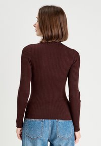 Bordeaux ribbet striktrøje med lange ærmer, høj krave, tætsiddende design og struktureret stof, parret med lys blå højhofte jeans.