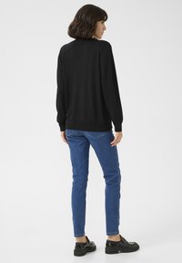 Haut à manches longues noir, avec des poignets et un ourlet côtelés, associé à un jean slim bleu et des chaussures à plateforme noires, vu de dos.