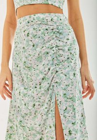 Floral maxi skirt in pastel colors, featuring a side slit and ruching detail with button accents, made from a lightweight, textured fabric.