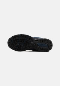 Suela de goma negra con patrón de relieve texturizado y acentos azules. Presenta surcos flexibles y un diseño contorneado para tracción y durabilidad.