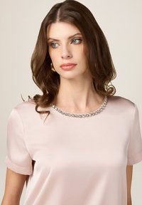 Blusa in satin rosa chiaro con maniche corte, scollatura rotonda e un bordo decorativo in strass attorno al collo. Tessuto liscio, design elegante.