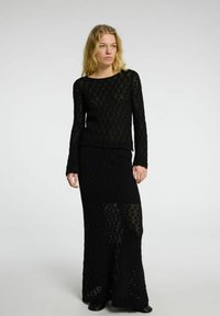 Set di vestito nero lavorato a maglia composto da un top a maniche lunghe con scollatura rotonda e una gonna maxi con un motivo a reticolo sfondato.